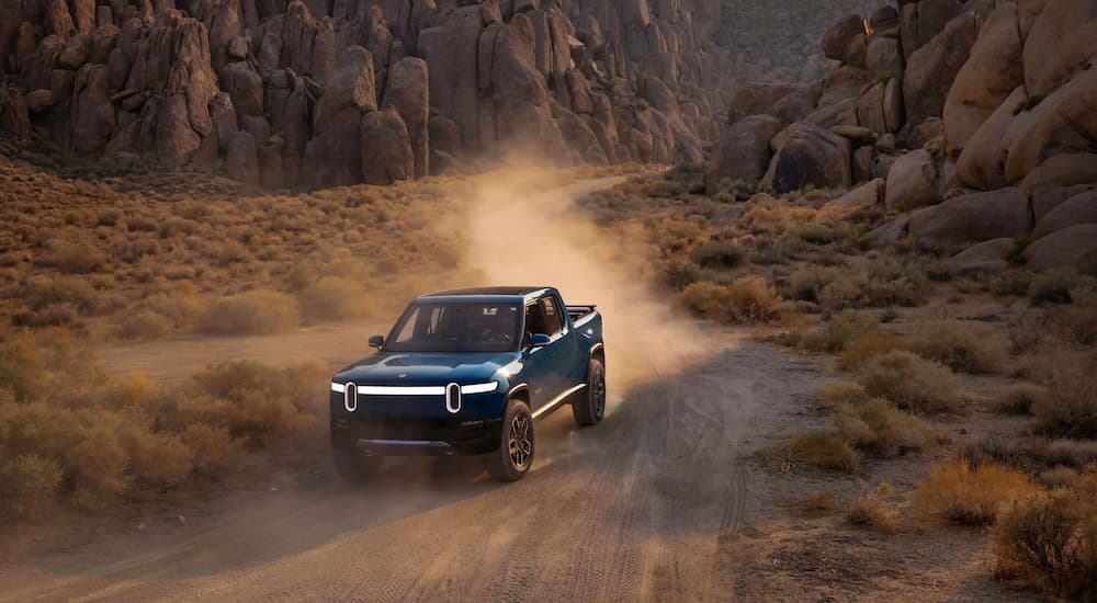 A blue Rivian R1T is shown driving on a dusty desert road.