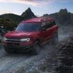 A red 2021 Ford Bronco Sport is shown from the front driving on a remote dirt road.