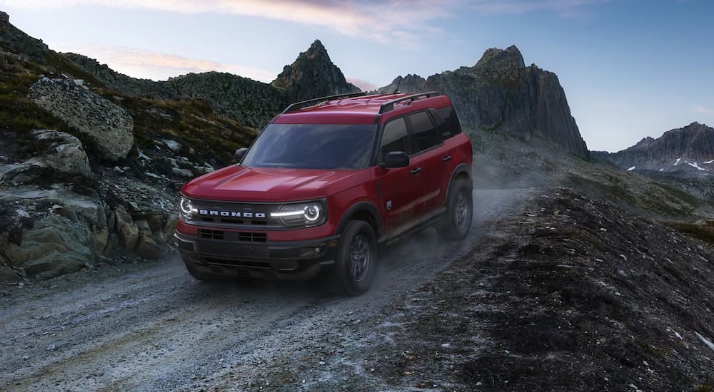 A red 2021 Ford Bronco Sport is shown from the front driving on a remote dirt road.