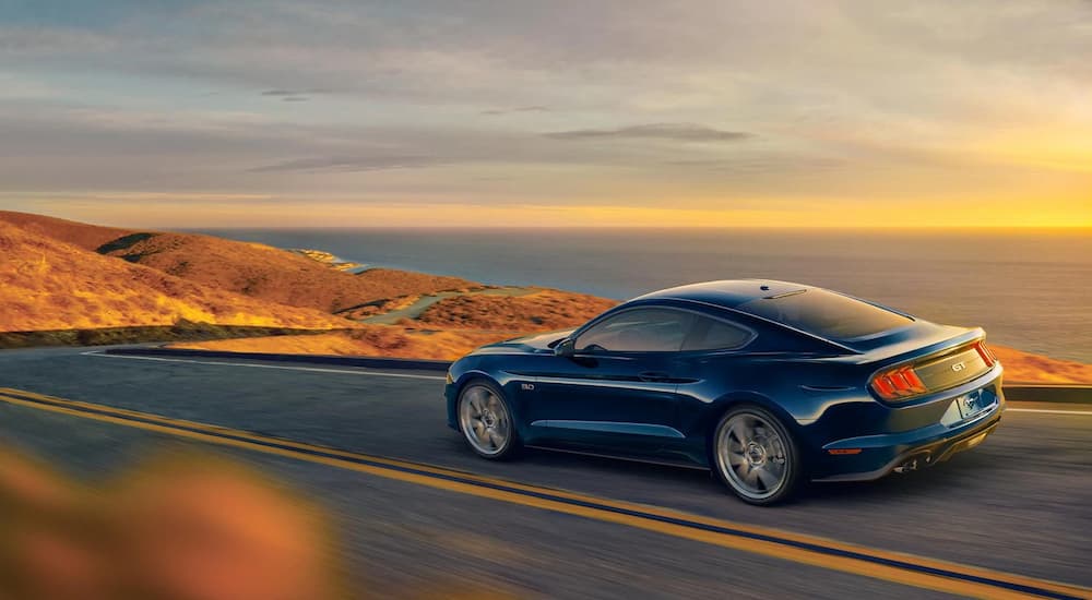 A 2021 blue Ford Mustang is shown driving near an ocean after looking at Ford lease deals.