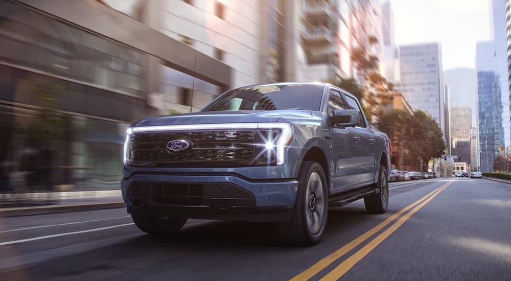 A blue 2022 Ford F-150 Lightning is shown driving through a city after leaving a Ford dealership.