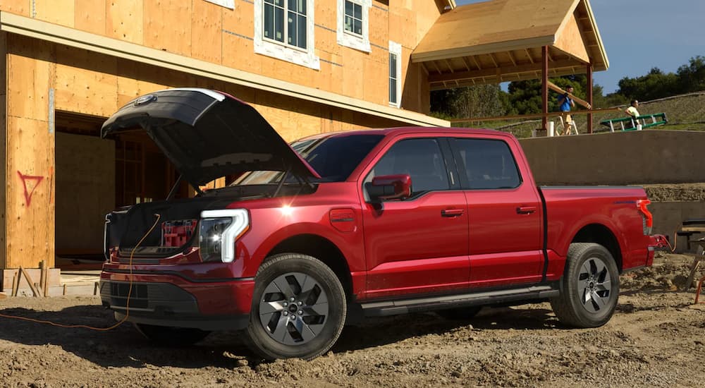 A red 2022 Ford Lightning is shown parked at a construction site with the hood being used to to store tools.