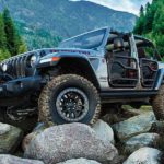 A silver 2021 Jeep Wrangler Rubicon is shown with the doors off while off-roading on a mountain path.