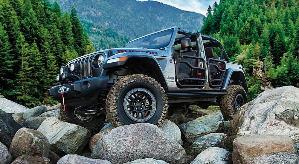 A silver 2021 Jeep Wrangler Rubicon is shown with the doors off while off-roading on a mountain path.