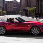 A red 2021 Mazda MX-5 Miata is shown from the side driving in a city.