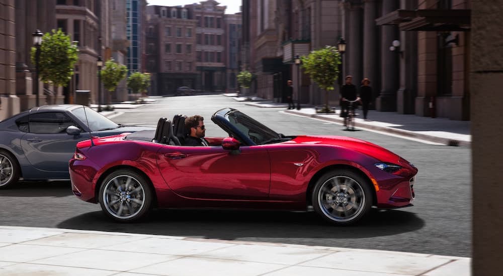 A red 2021 Mazda MX-5 Miata is shown from the side driving in a city.