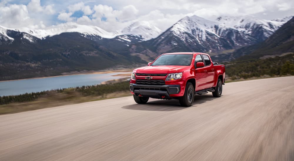 A red 2022 Chevy Colorado is shown from the front driving on an open road past a lake.
