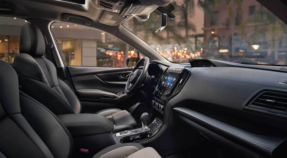 The black leather interior of a 2022 Subaru Ascent shows the infotainment screen, steering wheel, and front seats.