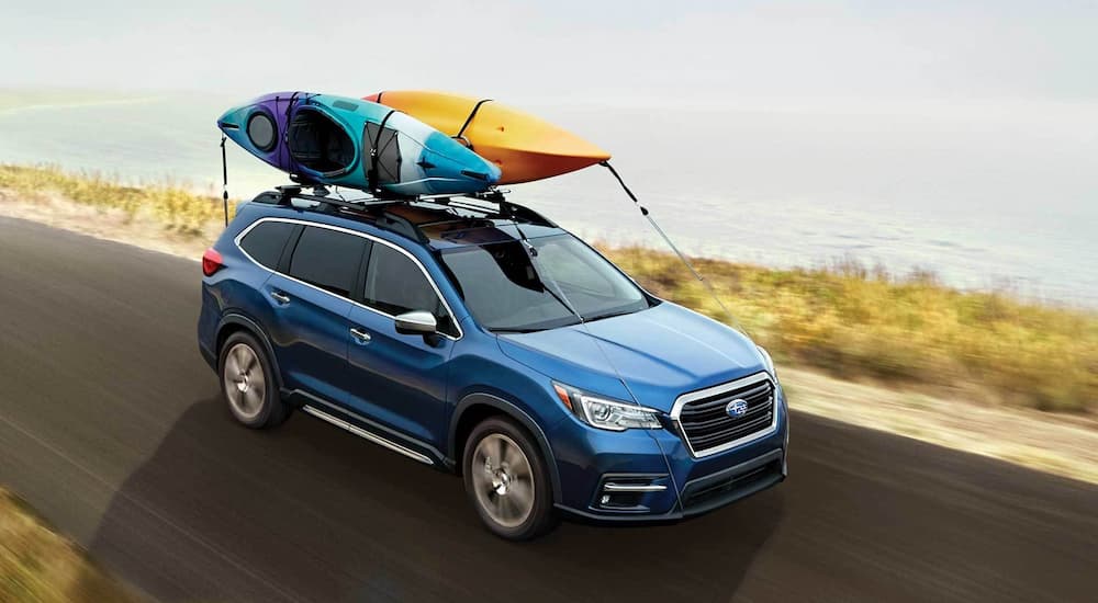 A blue 2022 Subaru Ascent with two kayaks on the roof rack is shown from a high angle driving by the ocean.