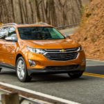 An orange 2018 Chevy Equinox is shown driving on a road after visiting multiple used car dealers.