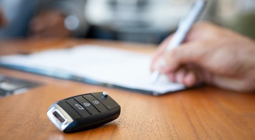 A person is signing paperwork next to a car key.