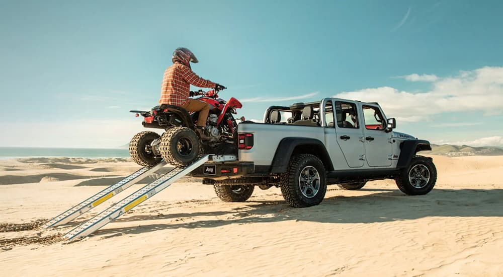 A man is shown driving an ATV into the bed of a white 2021 Jeep Gladiator Rubicon.