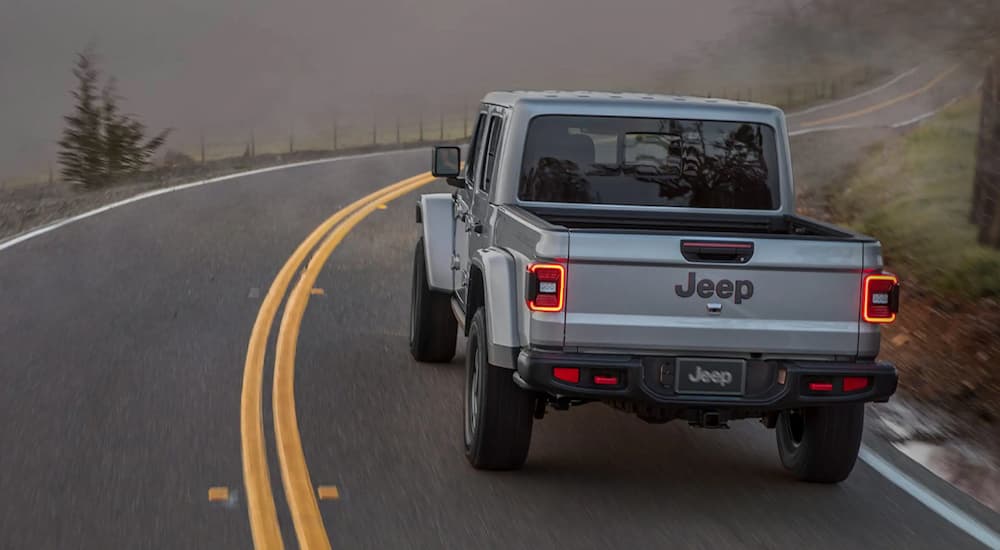 A silver 2022 Jeep Gladiator is shown from the rear driving on a foggy road.