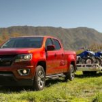 A red 2018 Chevy Colorado is shown towing a trailer through a grass field.