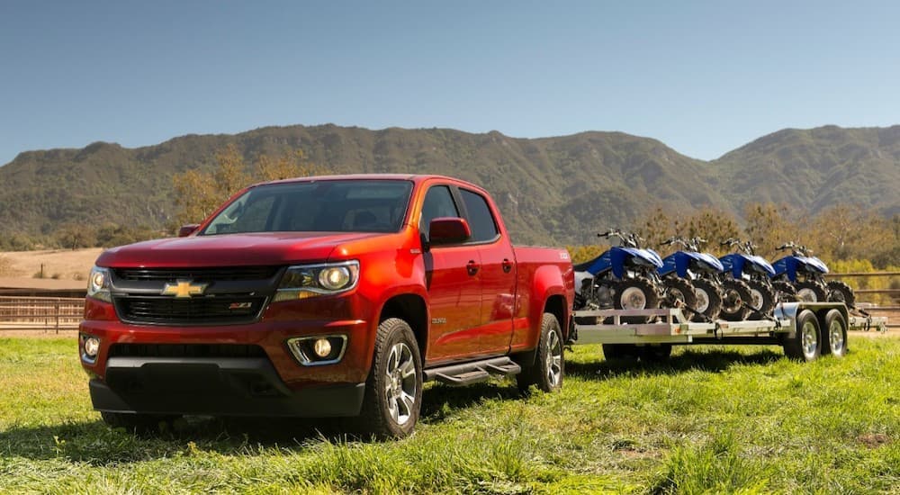 A red 2018 Chevy Colorado is shown towing a trailer through a grass field.