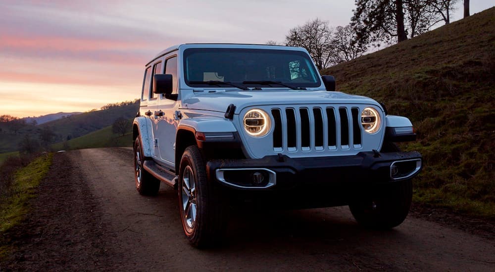 A white 2019 Jeep Wrangler is shown from the front driving at sunset.