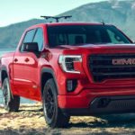 A red 2020 GMC Sierra 1500 is shown from the front parked in front of a lake after researching used trucks.
