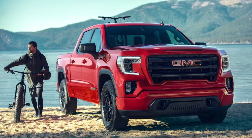 A red 2020 GMC Sierra 1500 is shown from the front parked in front of a lake after researching used trucks.