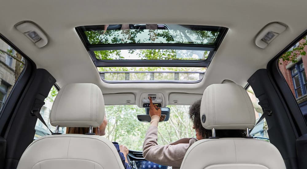 The white interior of a 2022 Buick Encore GX shows two people sitting in the front seats opening the moon roof.