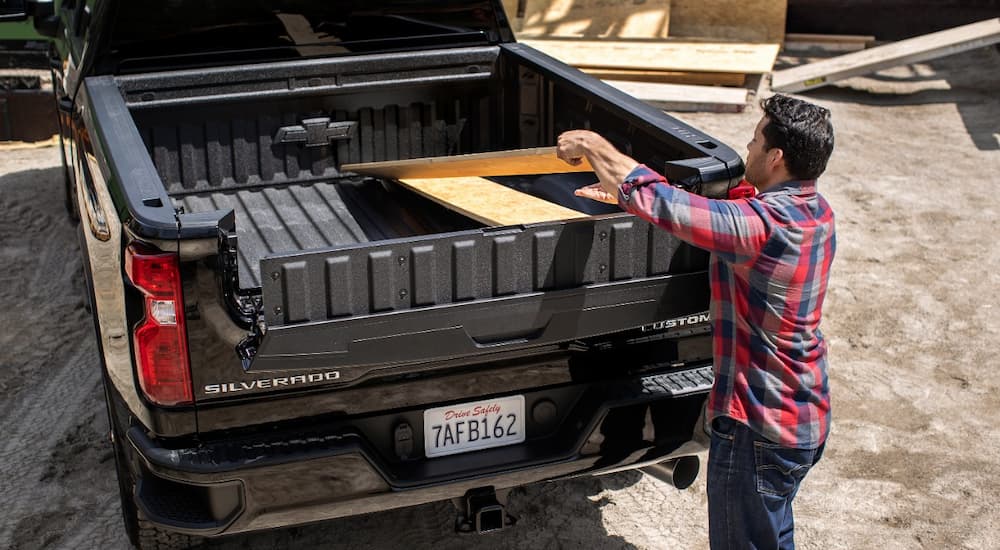 A man is shown putting boards into the bed of a black 2022 Chevy Silverado 2500HD.