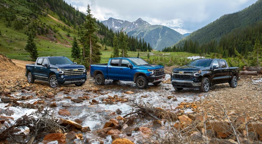 Three trim levels of the 2022 Chevy Silverado 1500 are shown parked in a low river.