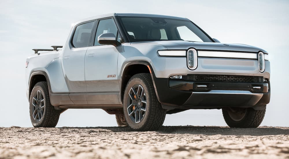 A silver 2022 Rivian R1T is shown parked in a sandy area.