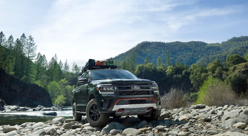 A green 2022 Ford Expedition Timberline is shown parked on rocks near a river.
