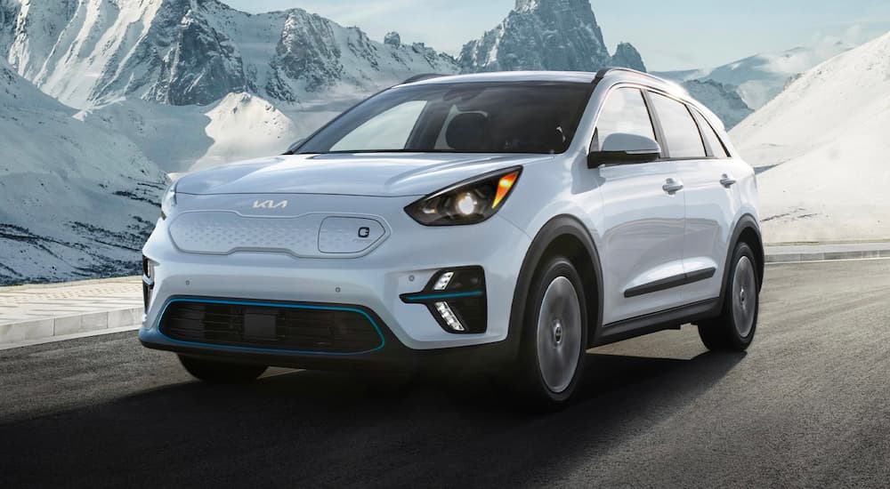 A white 2022 Kia Niro EV is shown driving on a highway near snow-covered mountains.