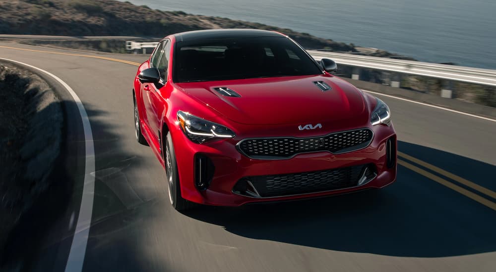 A red 2022 Kia Stinger GT is shown driving on a highway near a body of water.