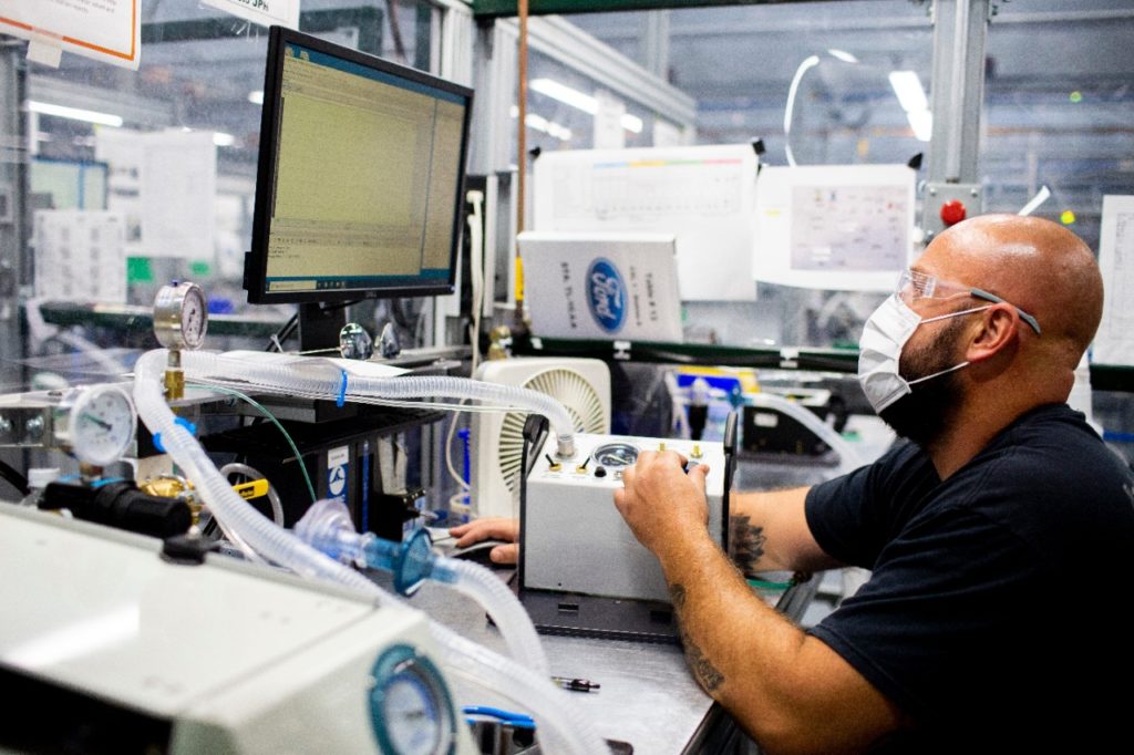 A man is shown putting together a ventilator at a Ford factory.