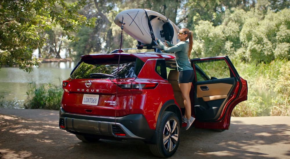 A woman is shown securing a kayak to the roof of a red 2021 Nissan Rogue Platinum.
