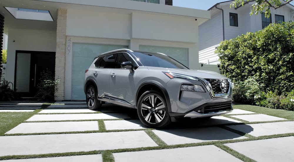 A silver 2021 Nissan Rogue is shown parked outside of a modern home.