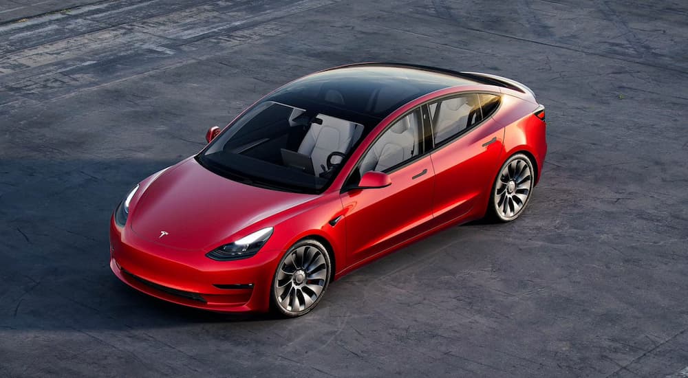 A red Tesla Model 3 is shown from a high angle parked in an empty lot.