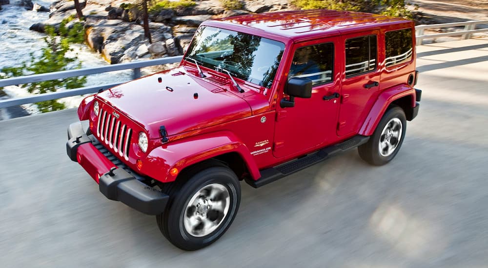 A red 2017 Jeep Wrangler Sahara is shown driving over a bridge.