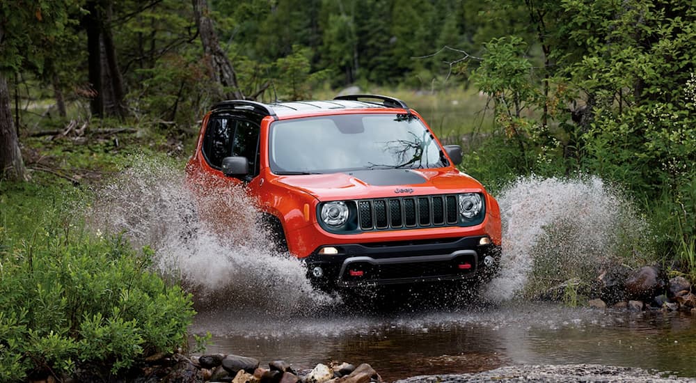 An orange 2019 Jeep Renegade is shown off-roading through a stream.