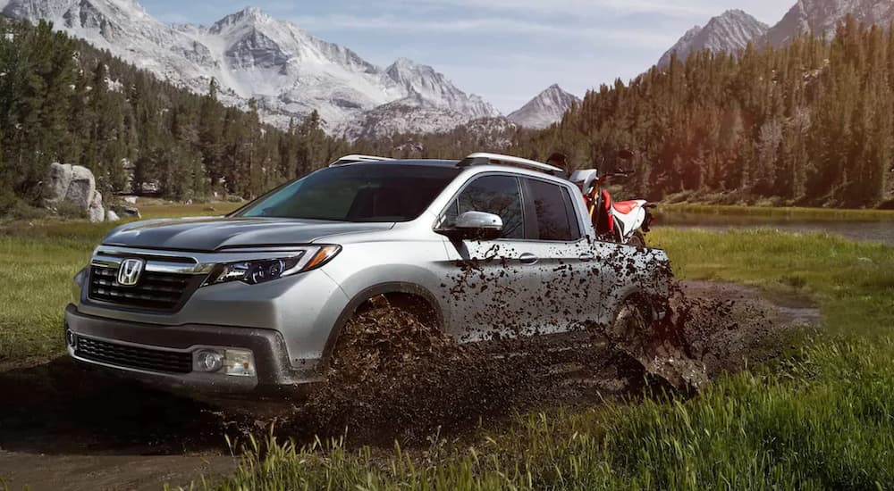 A silver 2020 Honda Ridgeline RTL-E is shown driving through a muddy field.