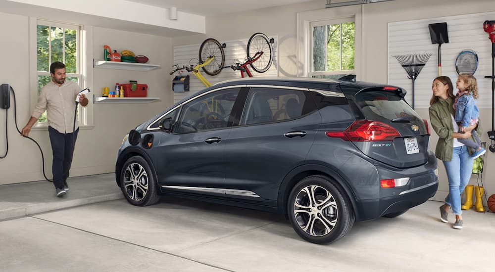 A family is shown charging a grey 2021 Chevy Bolt EV in a garage.