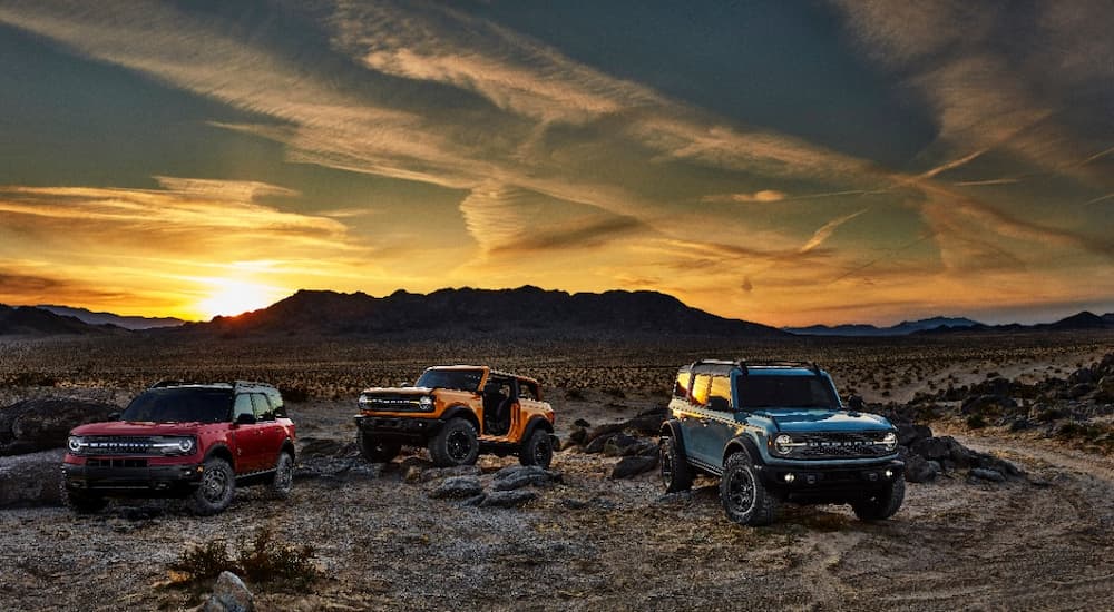 A red, an orange, and a blue 2021 Ford Bronco are shown parked in a desert area.