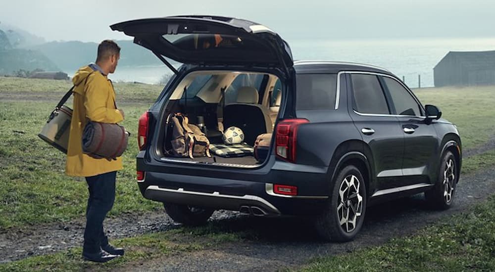 A man is shown putting bags into the rear cargo area of a grey 2021 Hyundai Palisade.