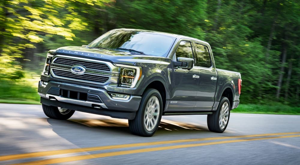 A grey 2021 Ford F-150 is shown driving on a road during a sunny day.