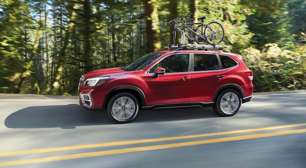 A red 2021 Subaru Forester is shown from the side driving on a road in a woodsy area.