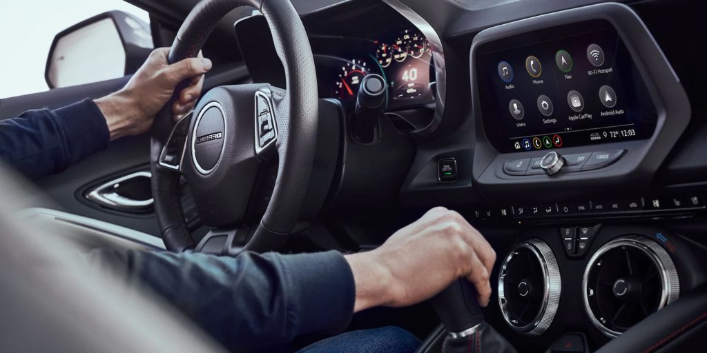 A close up shows a man driving a 2022 Chevy Camaro.