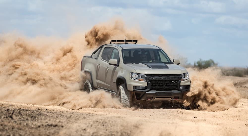 A tan 2022 Chevy Colorado ZR2 is shown off-roading in a dusty desert.