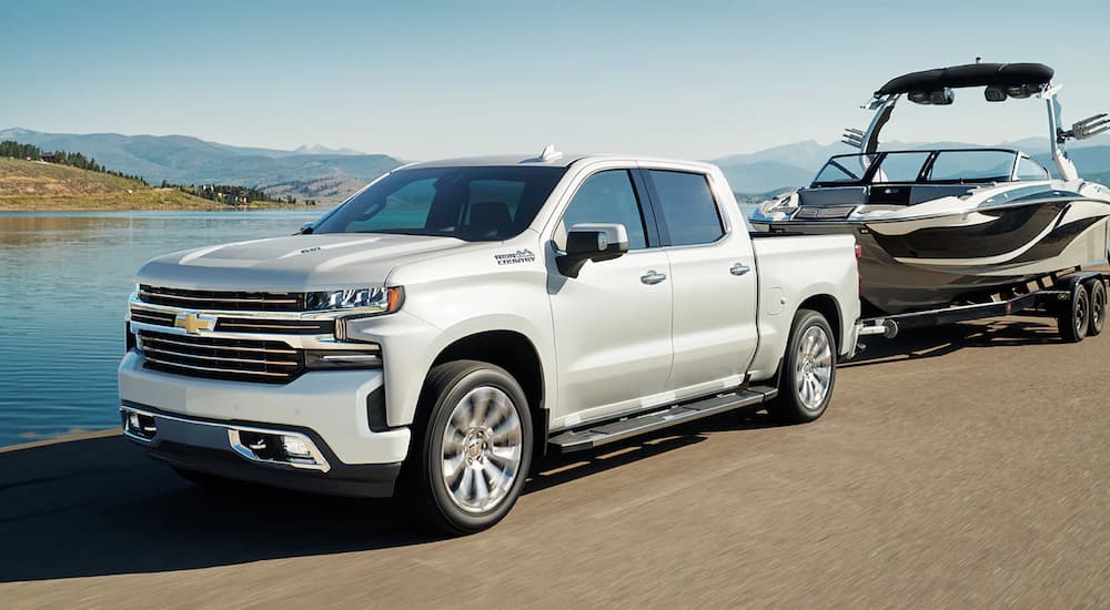 A silver 2022 Chevy Silverado 1500 High Country is shown towing a boat near a body of water.