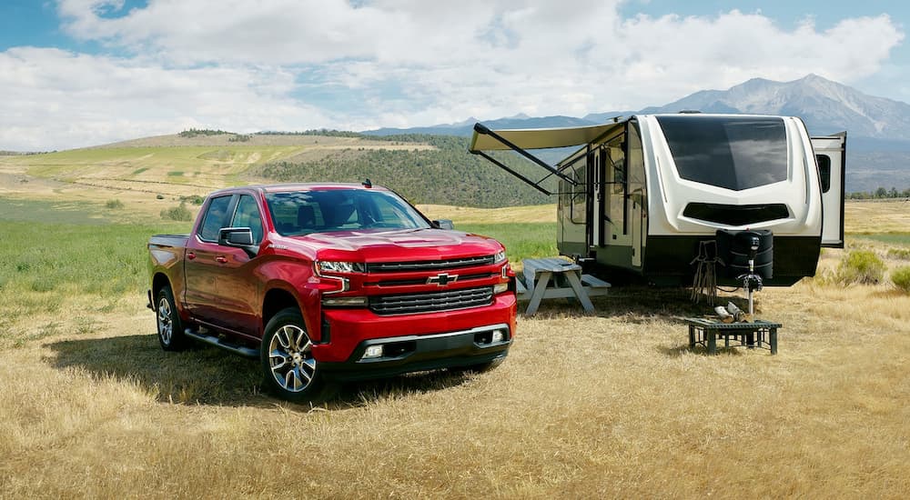 A red 2022 Chevy Silverado 1500 RST LTD is shown next to a camper in a dry grassy field.