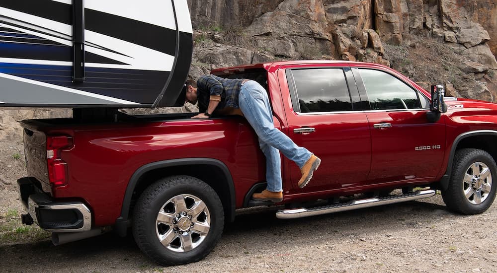 A man is shown checking the bed of a 2022 Chevy Silverado 2500 HD while towing a camper.