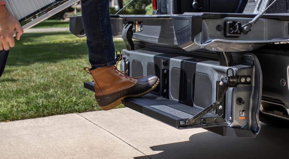 A close up shows a person stepping onto the multi-flex gate of a 2022 Chevy Silverado 2500 HD.