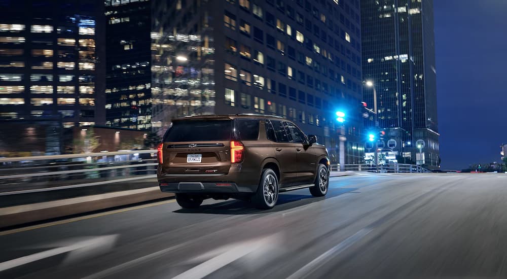 A brown A red 2022 Chevy Tahoe RST is shown from a rear angle driving in a city at night.