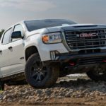 A white 2022 GMC Canyon AT4 is shown driving up a rocky road.