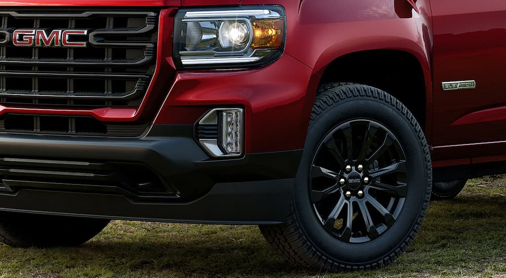 A close up shows the grille, headlight, and tire of a red 2022 GMC Canyon.